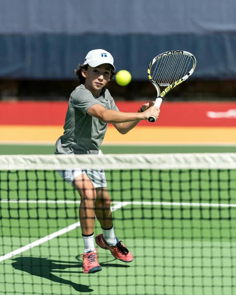 Junior tennis player driving a two-handed backhand at the net